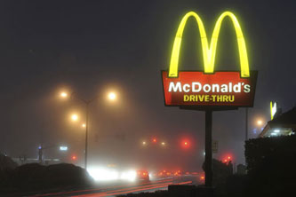 The McDonalds golden arches are seen on a foggy night by a road.