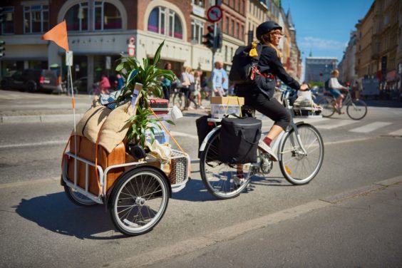 A person riding a Sladda Bike in the city while carrying a plant and various other objects